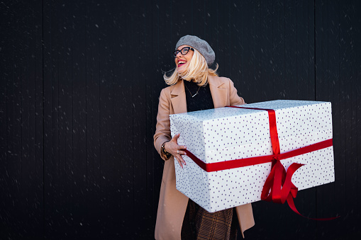 Portrait of happy woman walking outdoors with a big wrapped gift box.