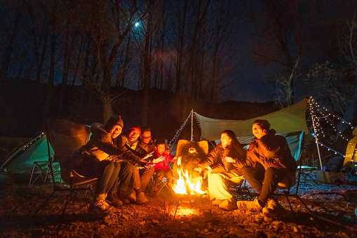 A group of campers celebrate around the campfire in late autumn night