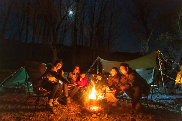 um grupo de campistas comemora ao redor da fogueira no final da noite de outono - bonfire people campfire men - fotografias e filmes do acervo