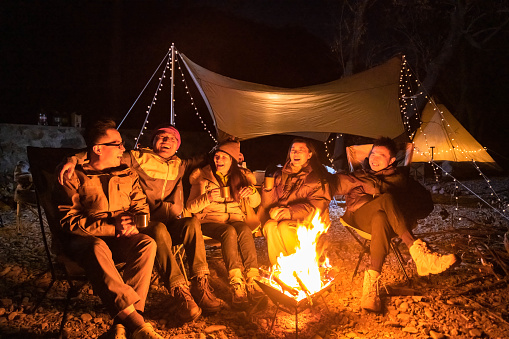 A group of campers celebrate around the campfire in late autumn night
