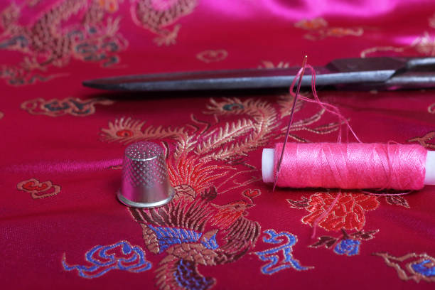 istock Spool of Pink Thread and Thimble on Vintage Pink Satin Fabric 1441602911