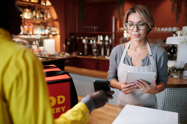 istock Focus on young waitress looking at screen of smartphone held by courier 1441604873