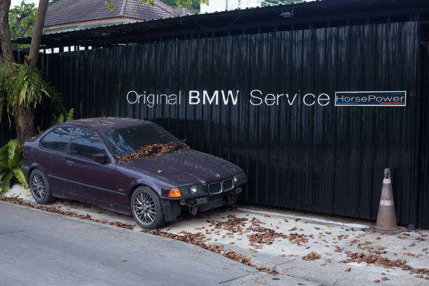 Weathered and at front damaged BMW car outside of local auto repair shop in Bangkok Ladprao Nakniwat area in old residential district. On metal wall are letters Original BMW service