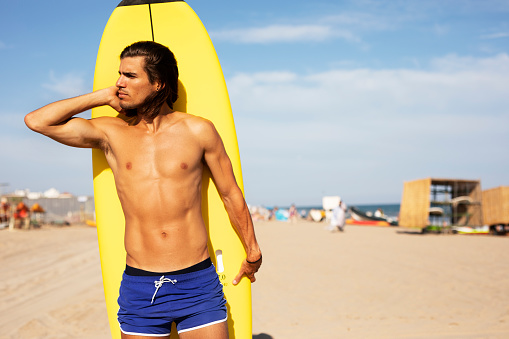 Portrait of handsome surfer with his surfboard. Young man with a surfboard on the beach.