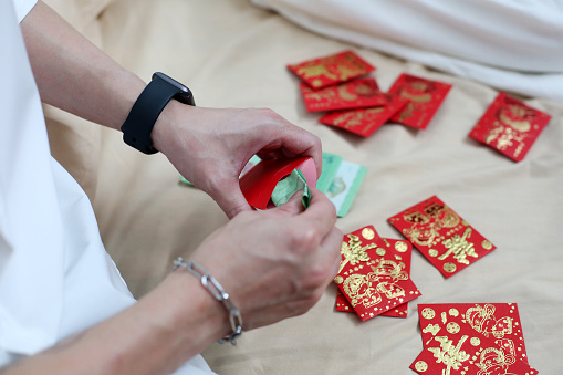 An Asian man is inserting red packets with Malaysian Ringgit banknotes.