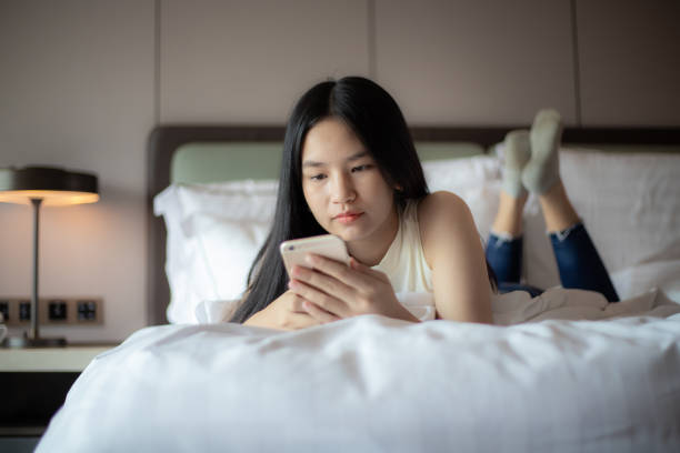 istock woman lying on white bed playing with phone 1441609917