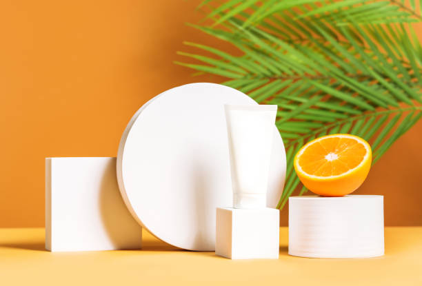 Front view mock up scene with unbranded white cosmetic tube on white podium and orange on a palm leaves background. Lotion, cream, hand cream, sunscreen, moisturizer mockup. stock photo