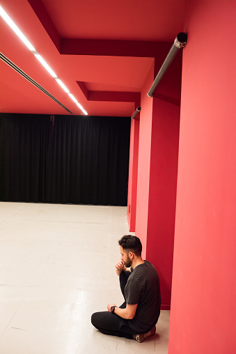 Young pensive bearded man sitting on the floor in red room