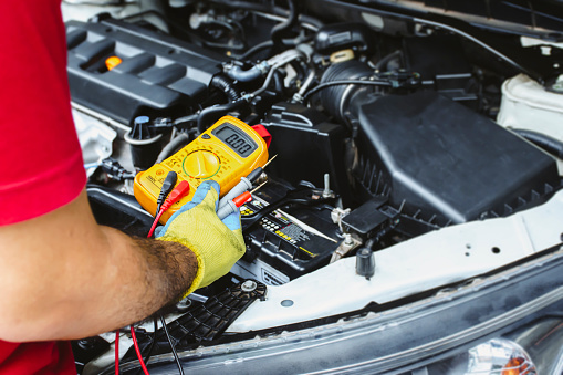 A mechanic holds a digital multimeter to check the car electrical system, auto maintenance service concept