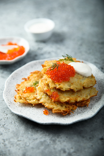 Close up view of potato pancakes. Potatoes pancakes latkes, flapjacks, hash brown or potato vada on gray plate over gray wooden table, with fresh parsley and sour cream. Copy space for text.
