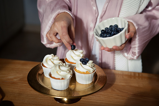 Close up of woman's hands cooking dessert cupcakes, decorate with berries