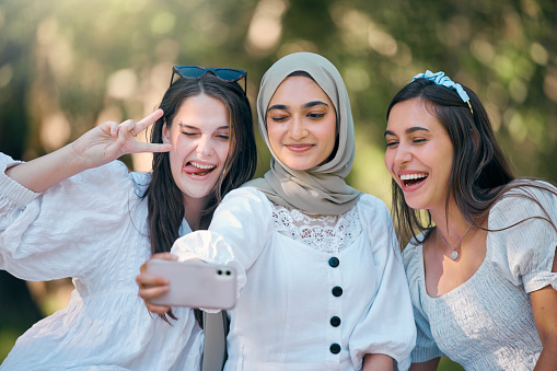 Selfie, phone and friends in nature park relax, bond and enjoy outdoor quality time together on spring day. Beauty, goofy or fun group of people, girl or women post picture to online social media app