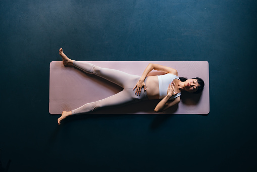 Directly above photo of serious Asian woman in sportswear lying down on a exercise mat at yoga studio.