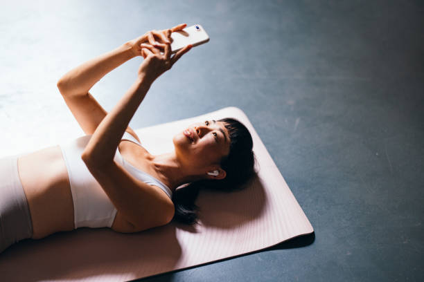 istock Smiling Woman With Wireless Earphones Lying On A Exercise Mat And Using Her Mobile Phone Before Workout 1441634802