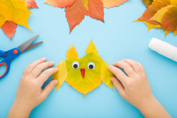 istock Little child hands creating owl shape from colorful leaves on light blue table background. Pastel color. Toddler development. Making autumn decorations. Point of view shot. Closeup. Top down view. 1441634906