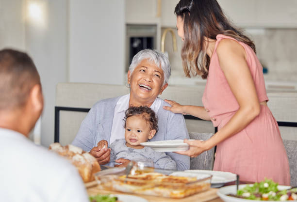 family, grandmother and baby with food at the dining room or kitchen table for mothers day. happy mother, father and grandma playing with newborn child with mother day lunch celebration or birthday - cooking senior adult healthy lifestyle couple imagens e fotografias de stock
