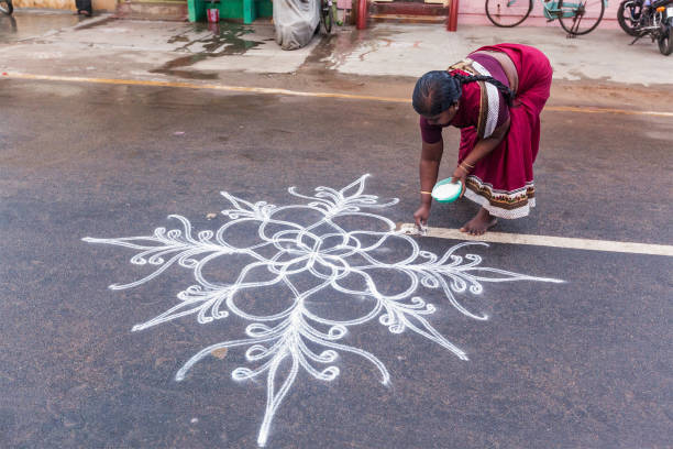 Unidentified India woman drawing Kolam (Rangoli) - form of painting drawn by using rice powder in front of the house - thought to bring prosperity to homes stock photo