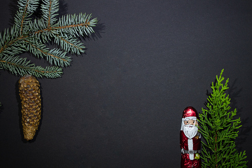 New Year backgraund - chocolate Santa Claus with a fir cone - with two christmas trees on a black background and empty space - and fir branch