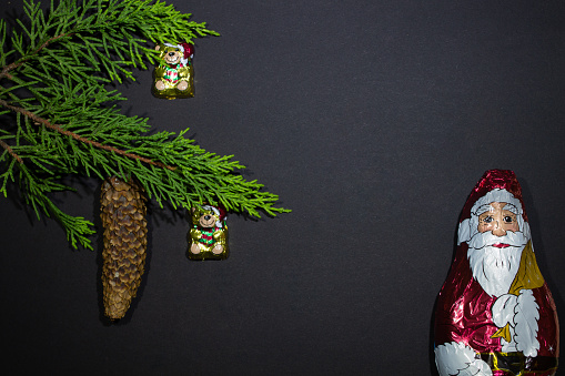 Christmas tree with a fir cone decorated with chocolate Christmas decorations - taddy bear - on a black background with and empty space - and big Chocolate Santa Claus