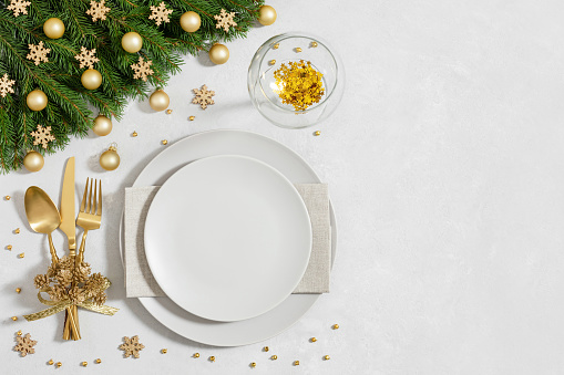 Christmas table setting with golden festive decorations and empty plate on a gray background. Happy new year. Space for text. Top view, flat lay.