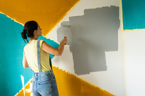 Woman decorating her living room, she is painting a wall with paint roller.