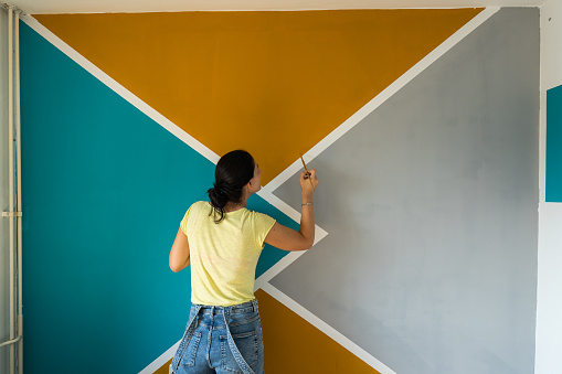 Woman decorating her wall at home, she is painting details with a paintbrush.