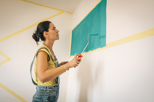 Woman decorating her living room, she is painting a wall with paint roller.