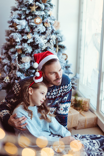 Father and daughter feeling sad for christmas , looking trough the window