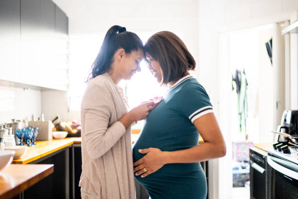 istock Lesbian couple looking each other while touching their heads in the kitchen at home - including a pregnant mid adult woman 1441645140