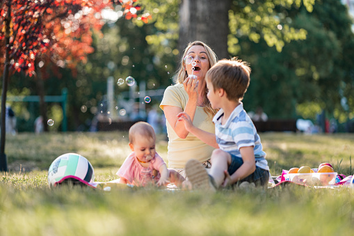 Mother blowing bubbles whit her children in the public park during summer day