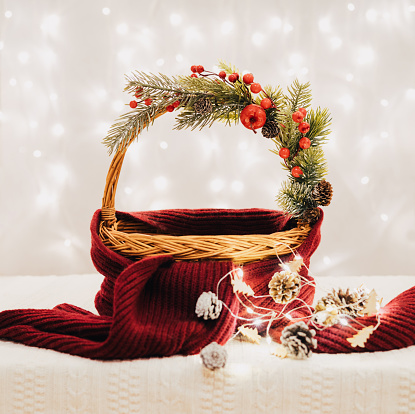 Christmas empty basket with festive decorations, glowing garland and scarf on a background of lights. Christmas design template. Happy new year.