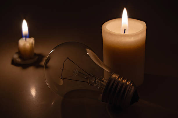istock Switched off light or not glowing light bulb near a burning candles in total darkness. Blackout city, electricity off, load shedding, energy crisis or power outage, concept image. 1441647787