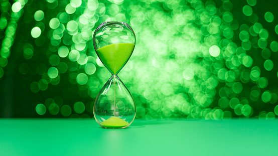 Modern hourglass on shiny green background.