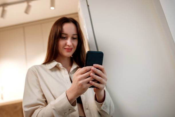 istock Happy woman freelancer in casual clothes using phone while standing on home kitchen during work brake 1441651307