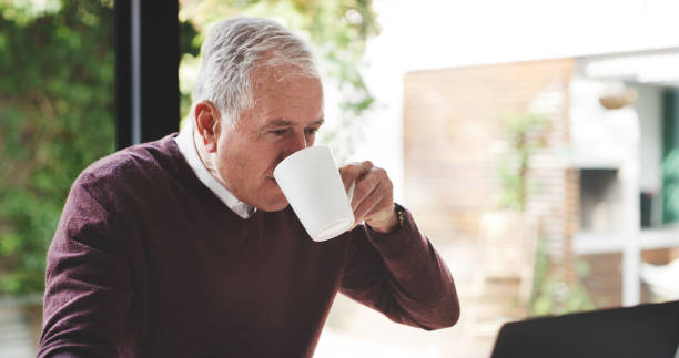 istock Senior man, coffee and sitting at laptop to relax during retirement while drinking tea, enjoying freedom and home wifi browsing internet. Elderly male with hot beverage as motivation to start morning 1441657863