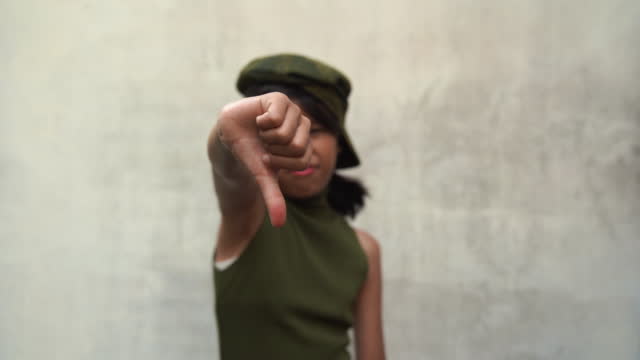 Asian teenage hipster girl posed thumbs down , white old wall background