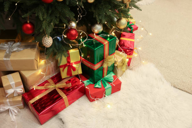 istock Decorated Christmas tree, beautiful gift boxes and festive lights on carpet 1441660339