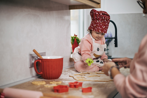 Mother love is shared to daughter while making cookies in kitchen encounter. Baby girl dressed as little chef is helping mom, while learning how to become successful at cooking.
