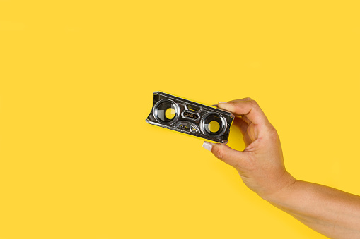 Woman hand holding a pocket magnifying glasses on a yellow background with copy space