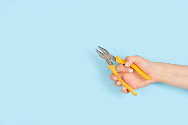 istock Woman hand holding a linesman’s pliers on a light background 1441661312