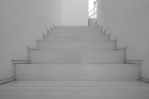 An outside staircase runs diagonally along the house wall and casts shadows on the wall and the paved floor - in black and white.