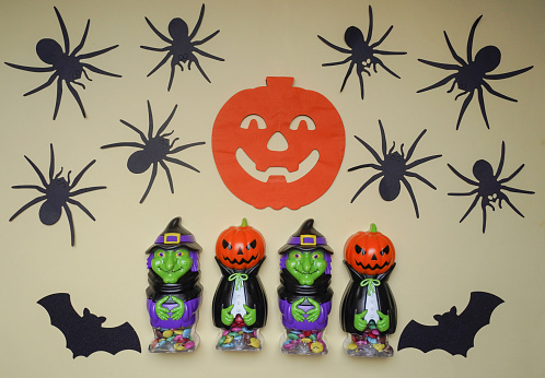 Scary Halloween figurines stand on a light background in close-up, behind hangs terrible pumpkin. Cute character in monster costume. Halloween concept. Holiday decorations toys