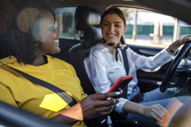 Young woman driving while her frined is looking up direction on a map via smart phonepassenger seat stock photo