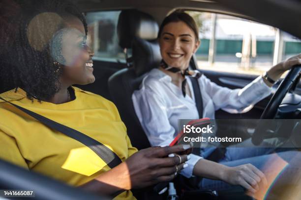 Young Woman Driving While Her Frined Is Looking Up Direction On A Map Via Smart Phonepassenger Seat Stock Photo - Download Image Now