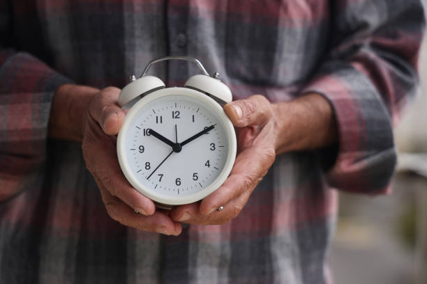 ein alter mann hält einen wecker in der hand - number alarm clock clock hand old fashioned stock-fotos und bilder