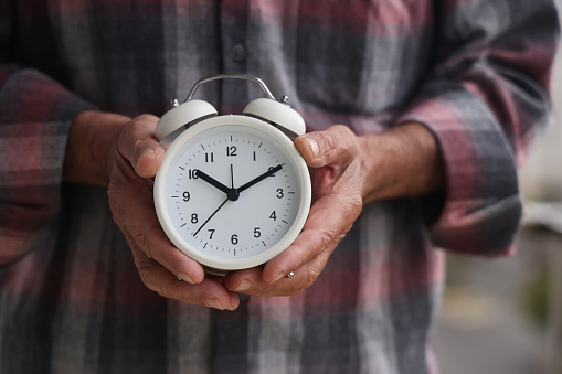 An old man is holding an alarm clock and time passes very fast