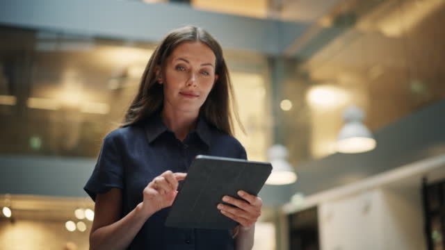 Female Data Analyst Smiling While Checking New Data for the Day. Portrait of White Businesswoman Walking Towards her Business Office in a Spacious Corporate Building. Low Angle, Slow Motion