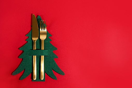 Christmas table place setting. Golden fork and knife with green christmas tree on red background, copy space