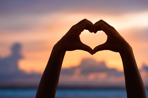 Woman hands forming a heart shape with sunset silhouette