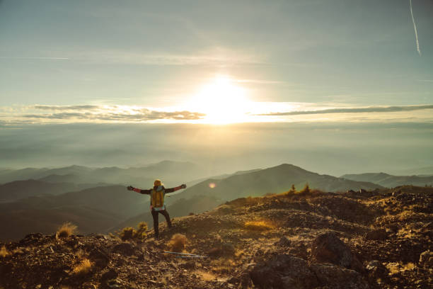 Female mountaineer stands arms outstretched on mountain top stock photo
